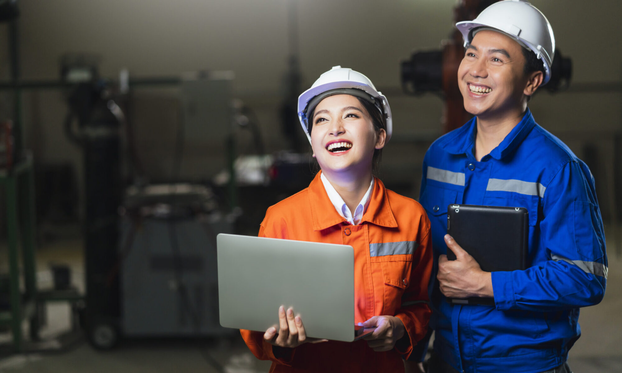portrait of asian emgineer male female technician in safty uniform standing and turn around to look at camera and laugh smile with cheerful and confident in machinery factory workplace background